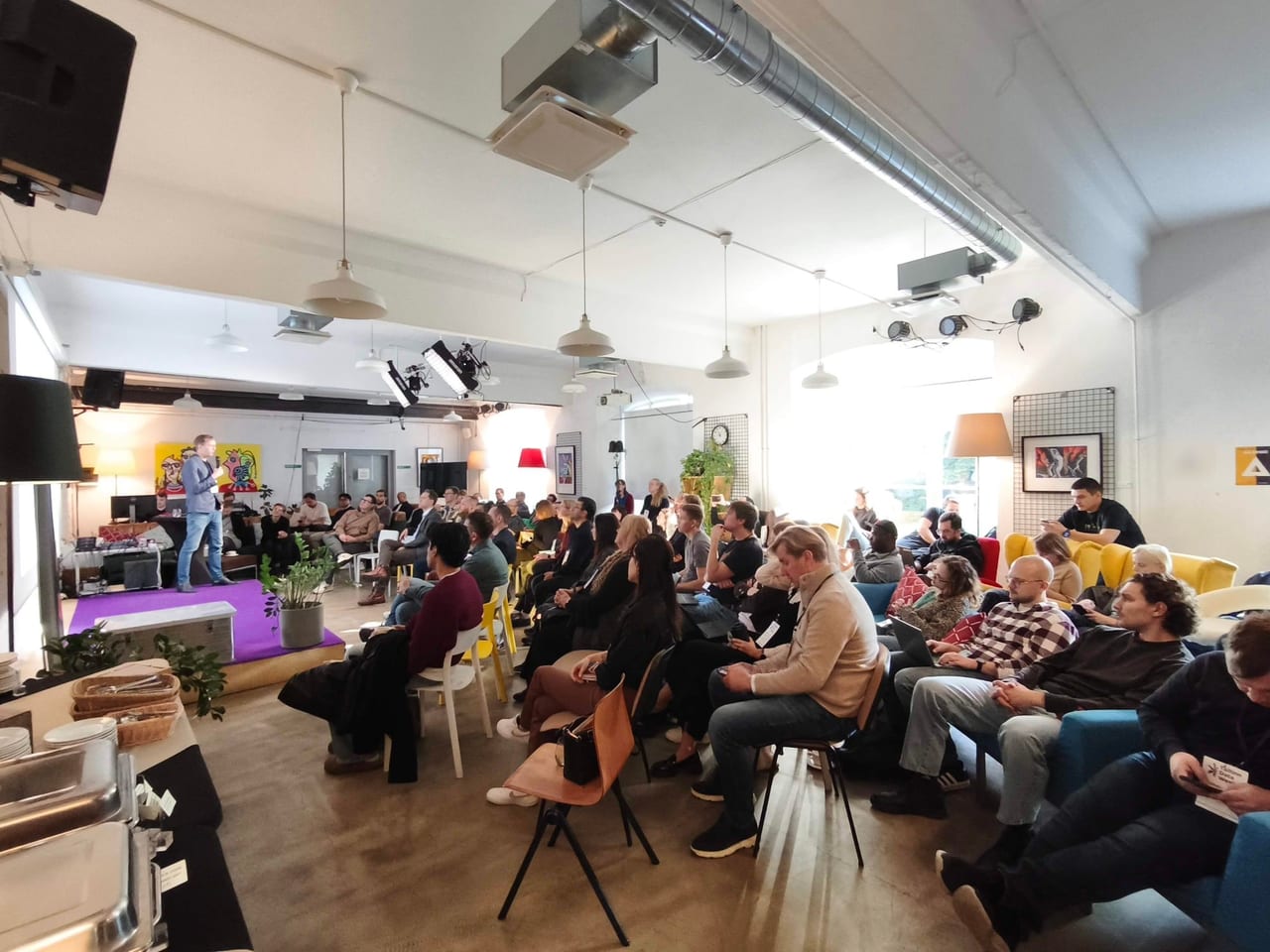 Täis saal Palo Alto Clubis Pieter Janseni ettekande ajal: Pieter räägib lillal laval, kuulajad istuvad toolidel ja diivanitel.